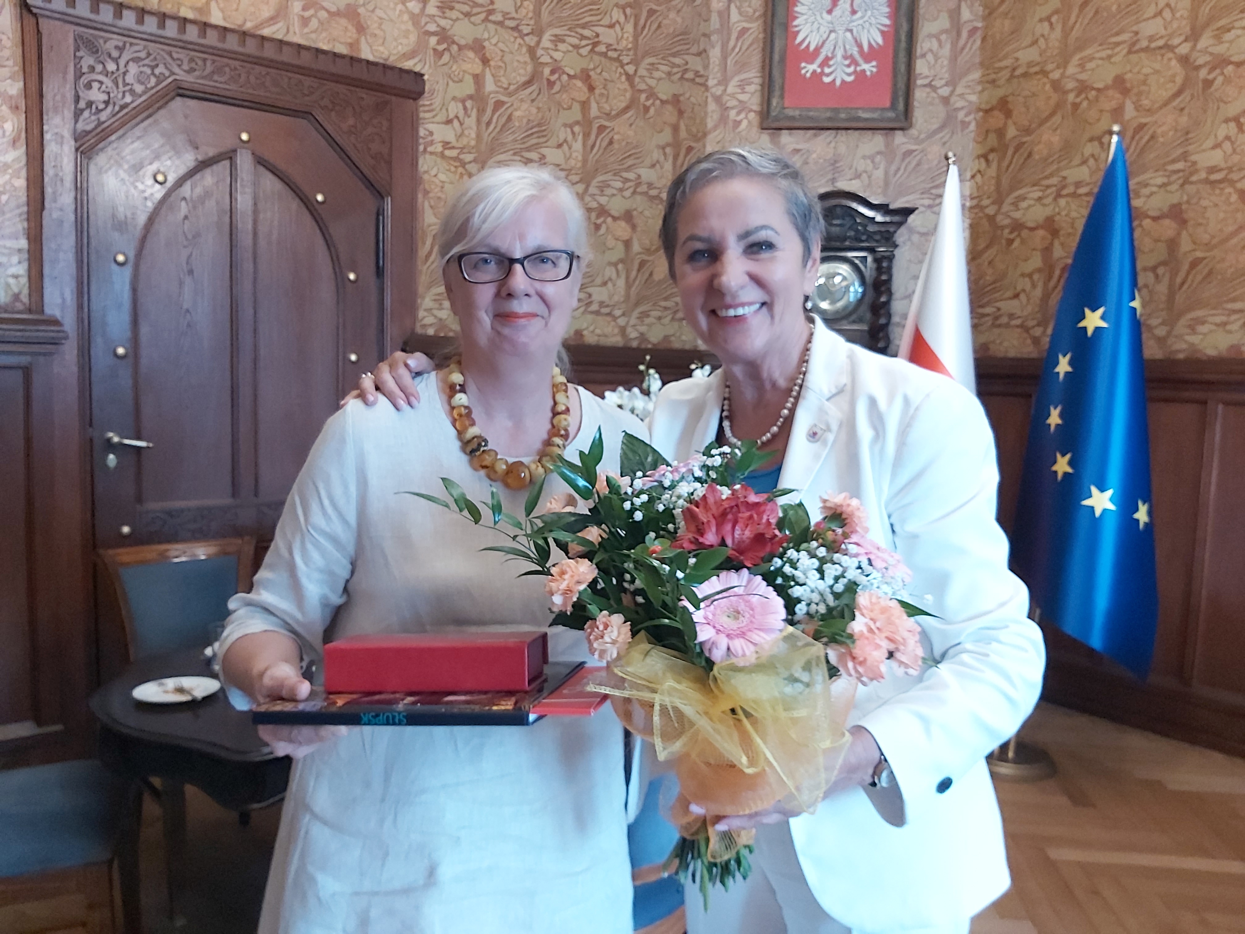 Katarzyna Zabawa trzymająca Album o Słupsku i pióro w pudełku z Prezydentką Słupska Krystyną Danilecką-Wojewódzką trzymającą kwiaty