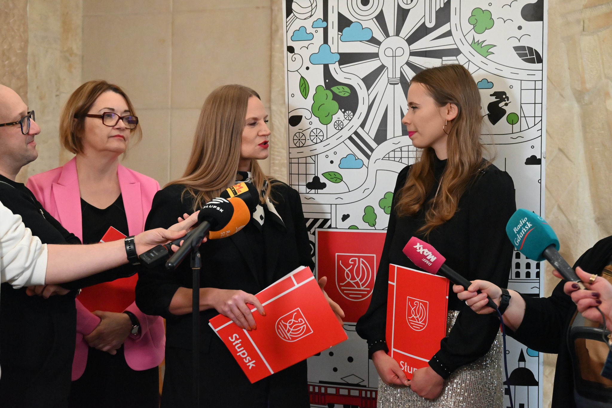Trzy kobiety stoją  przed nimi mikrofony przedstawicieli mediów