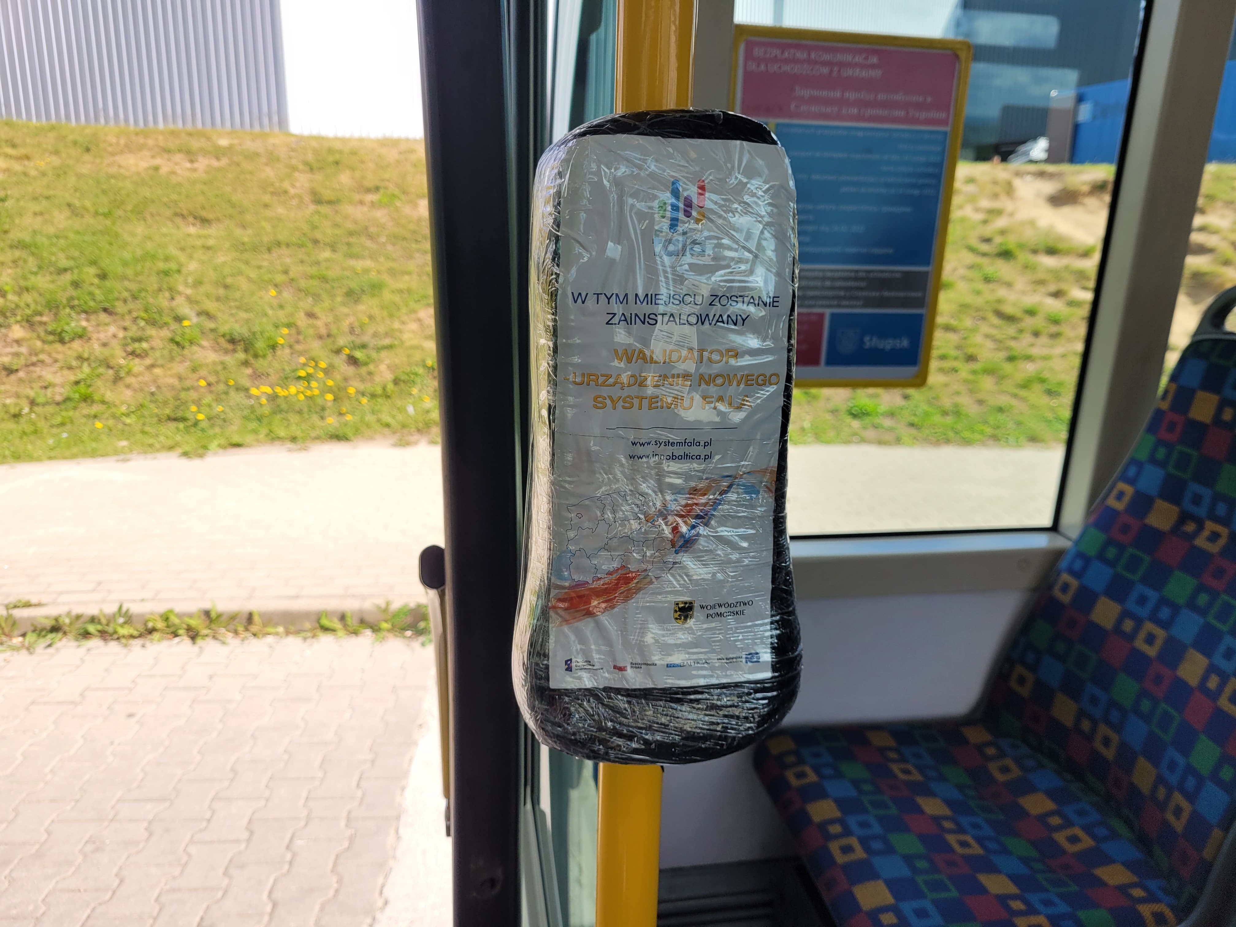 Na zdjęciu widzimy wnętrze autobusu miejskiego- siedzenia i uchwyty oraz  zafolionwany holder.