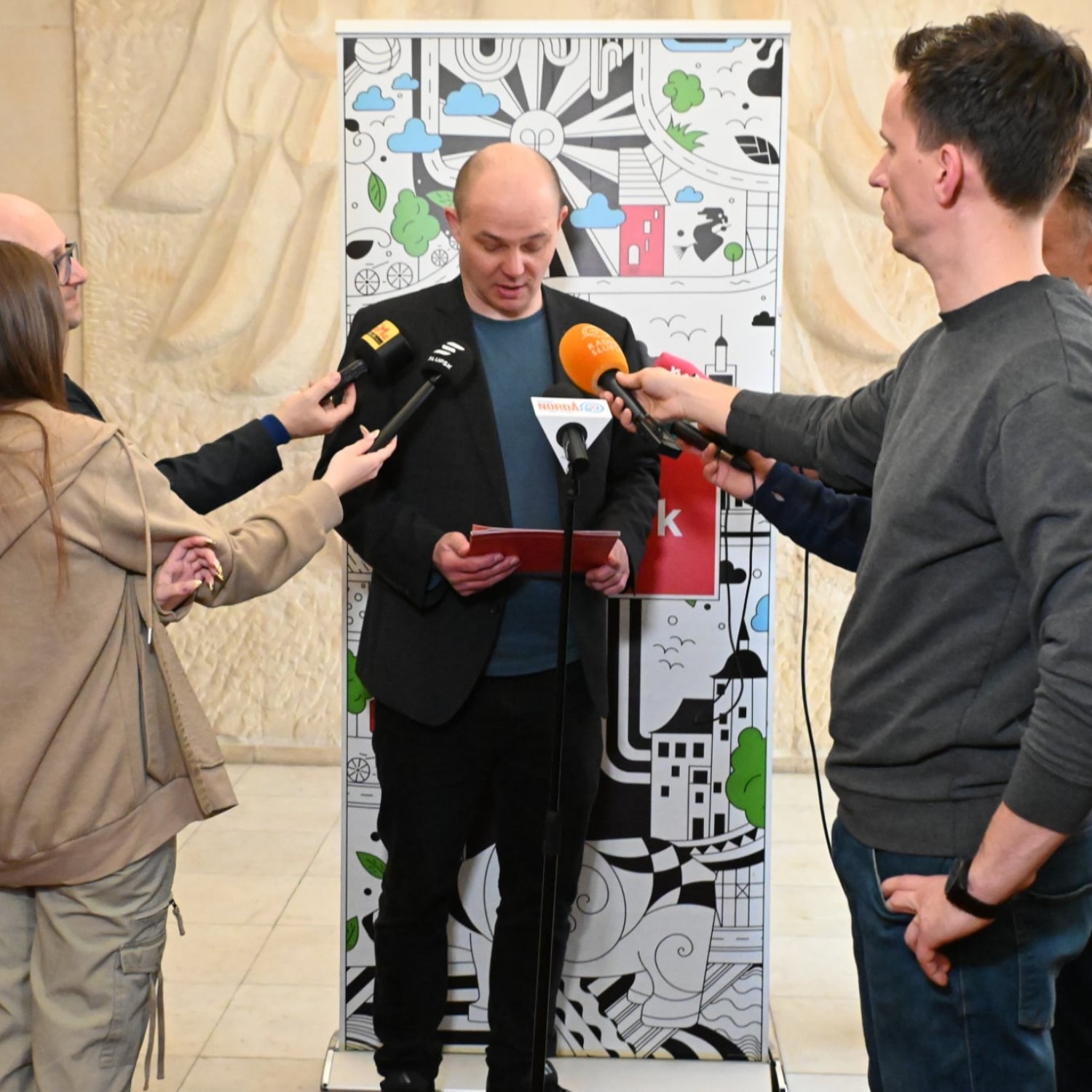 Mężczyzna stoi, przed nim mikrofony przedstawicieli mediów trzyma w dłoni czerwony dyplom