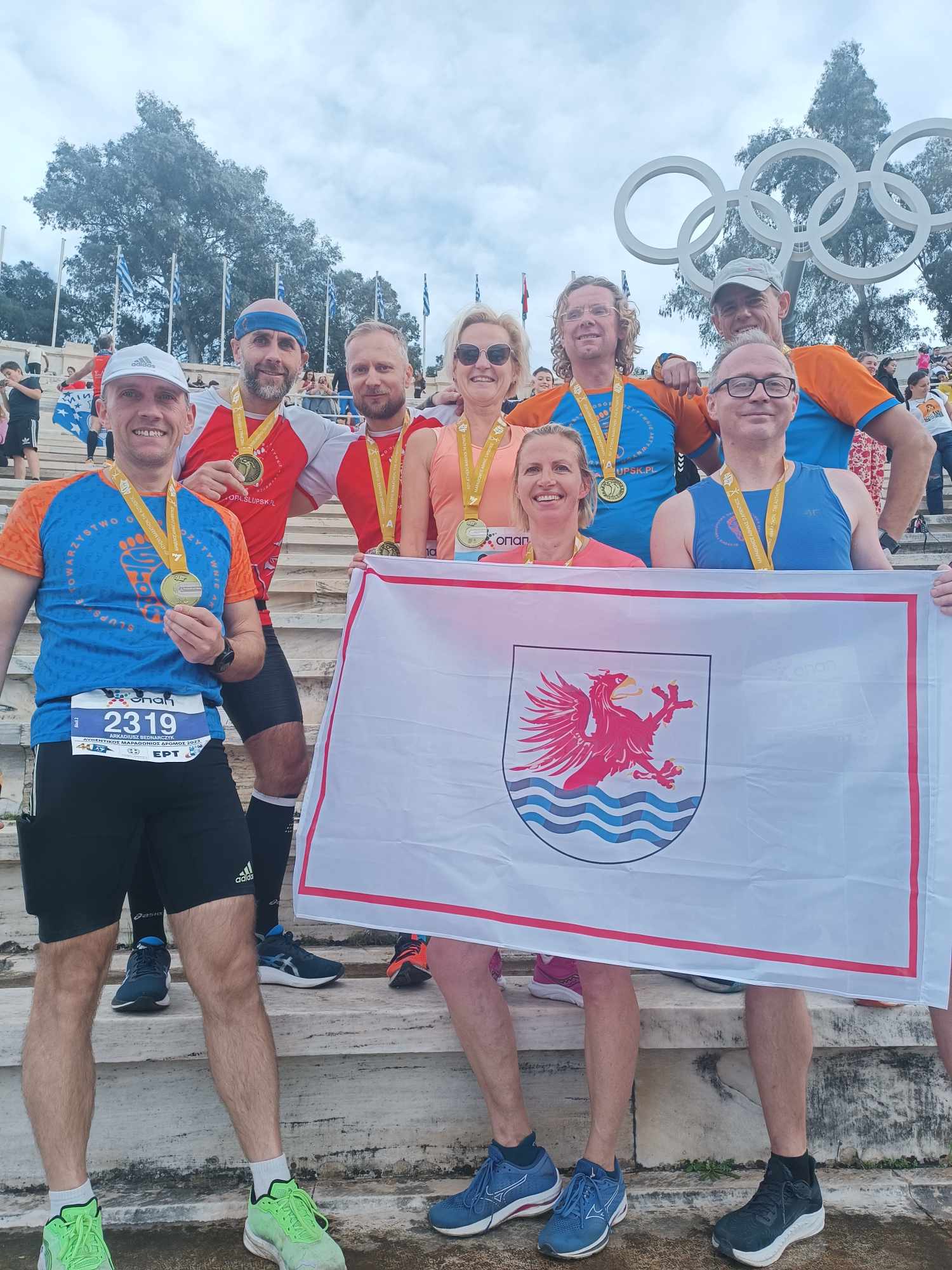 8 osób, biegaczy, trzymających flagę miasta Słupska na stadionie