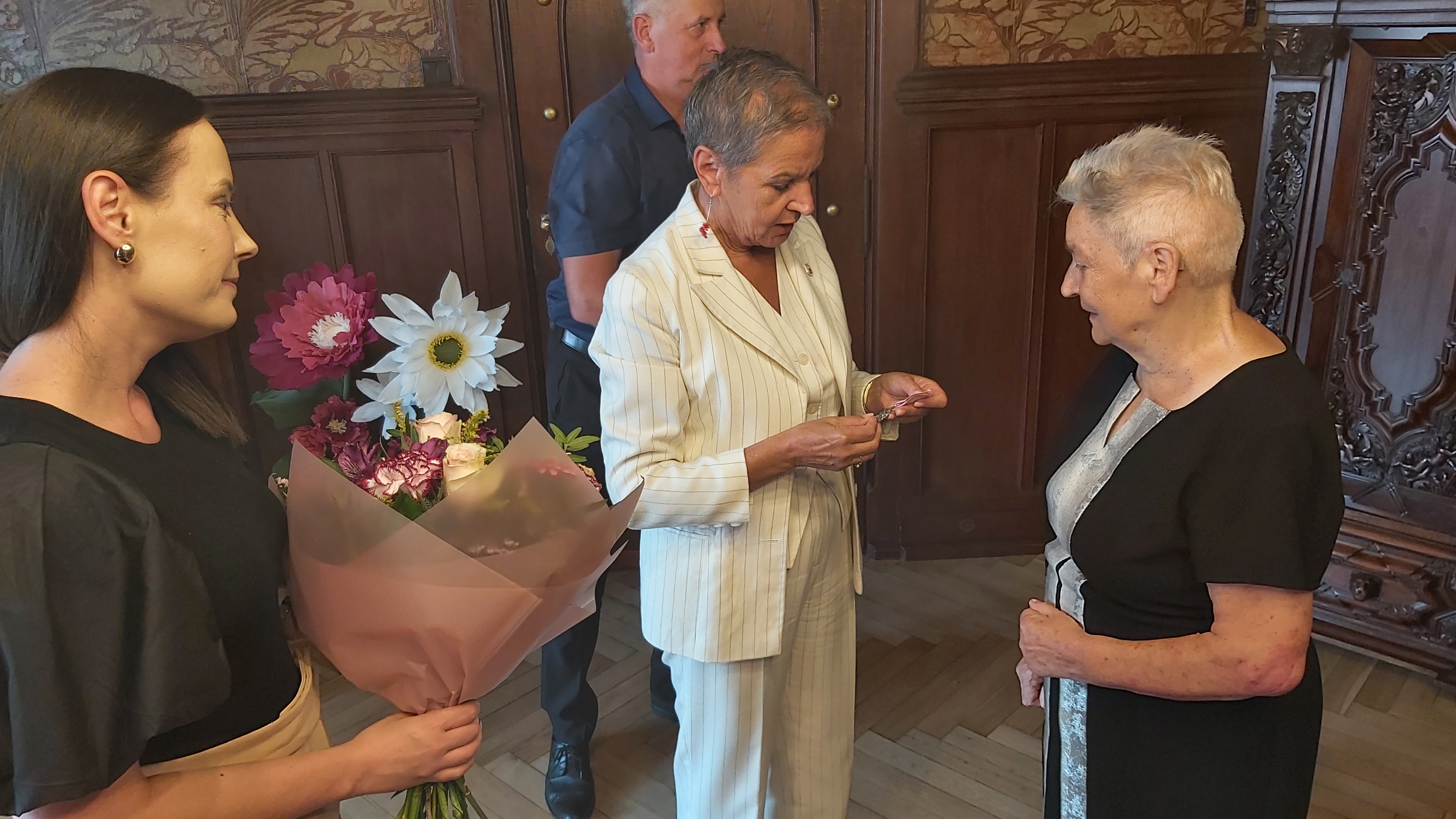 Prezydentka wręcza medal Jubilatce, Kierownik USC trzyma bukier kwiatów