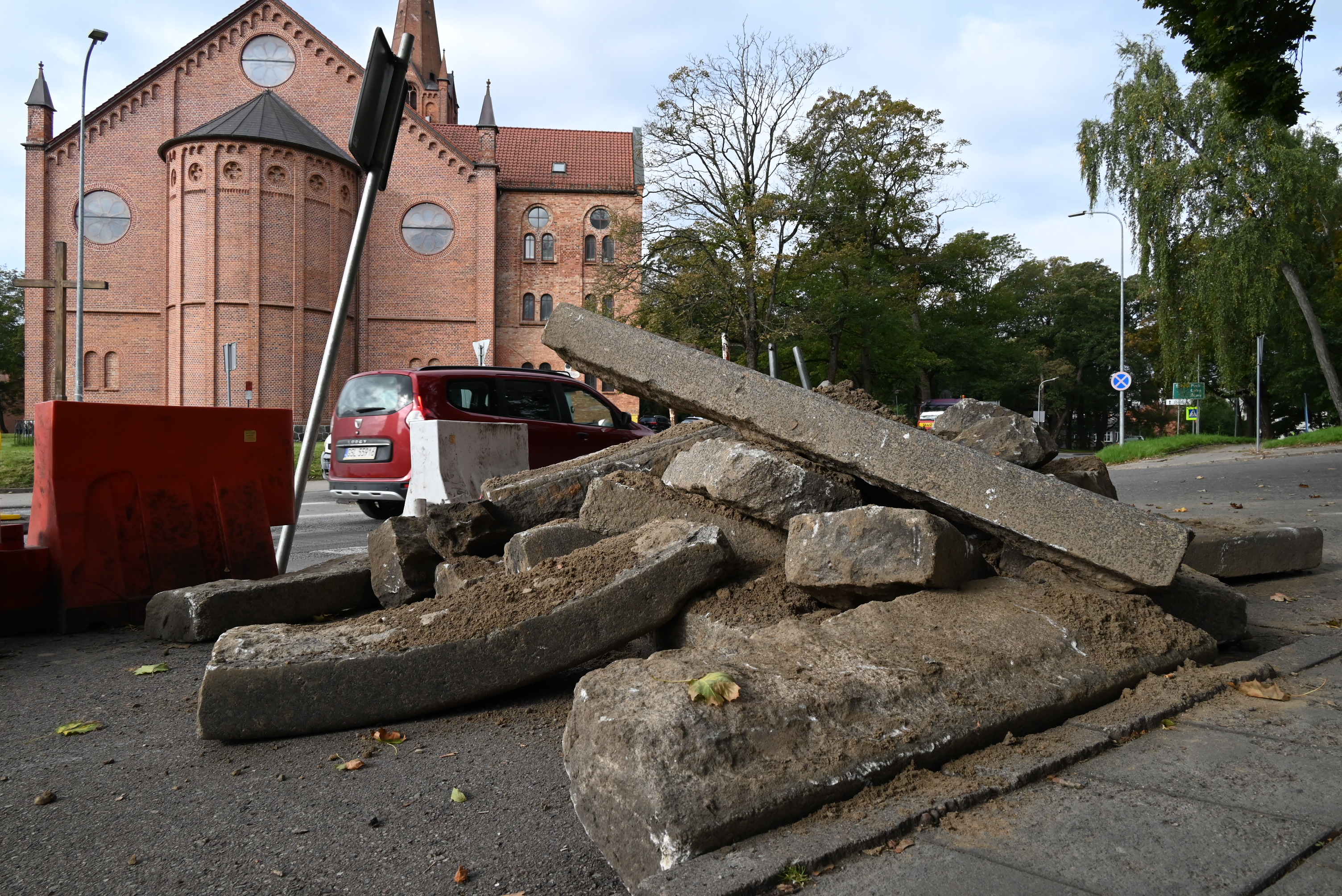 bloki betonu zerwane ułożone jeden na drugim, blokady wskazujące na brak możliwości wjazdu na dany fragment ulicy, w tle kościół i zabudowania w mieście
