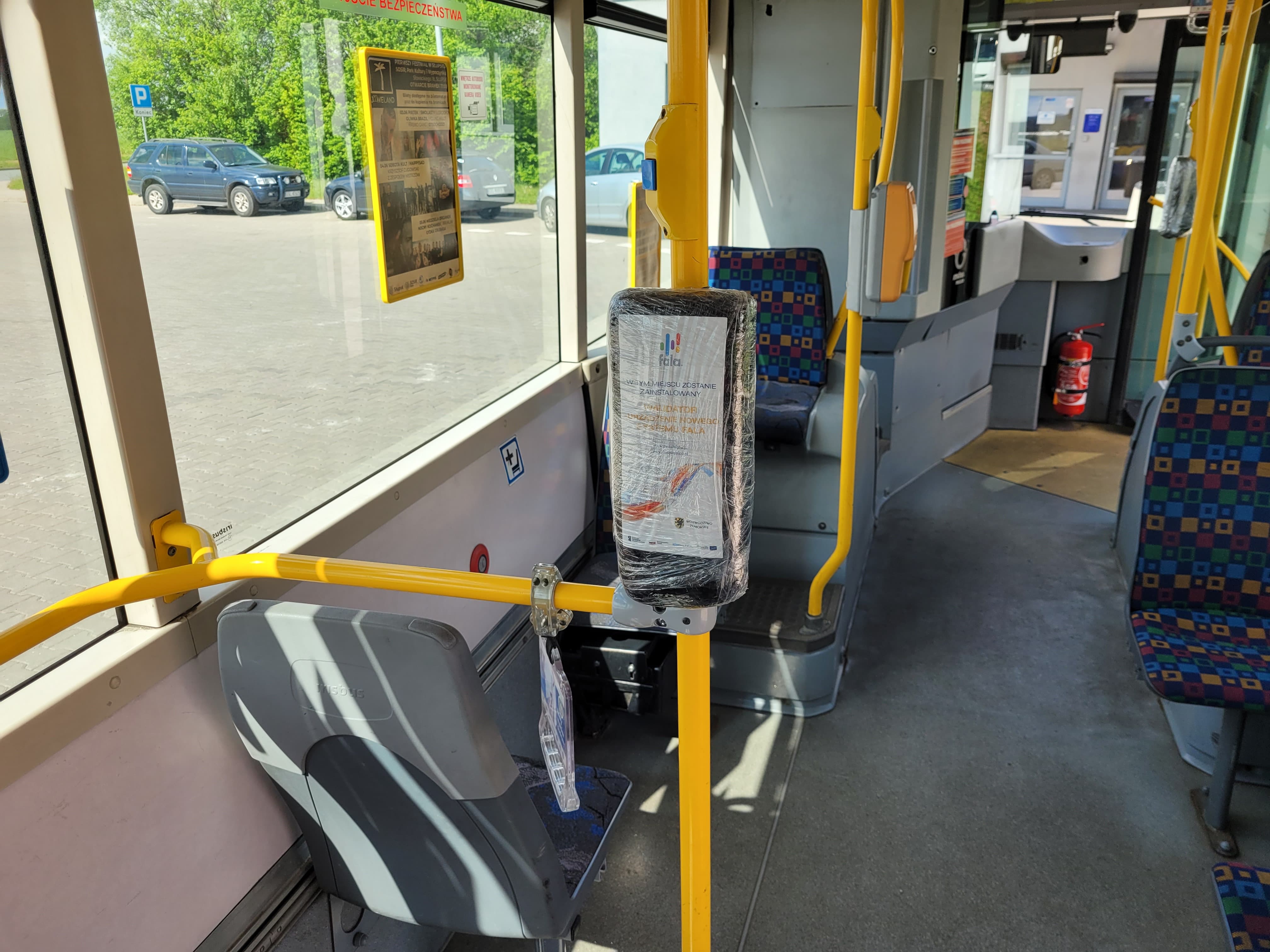 Na zdjęciu widzimy wnętrze autobusu miejskiego- siedzenia i uchwyty oraz  zafolionwany holder.