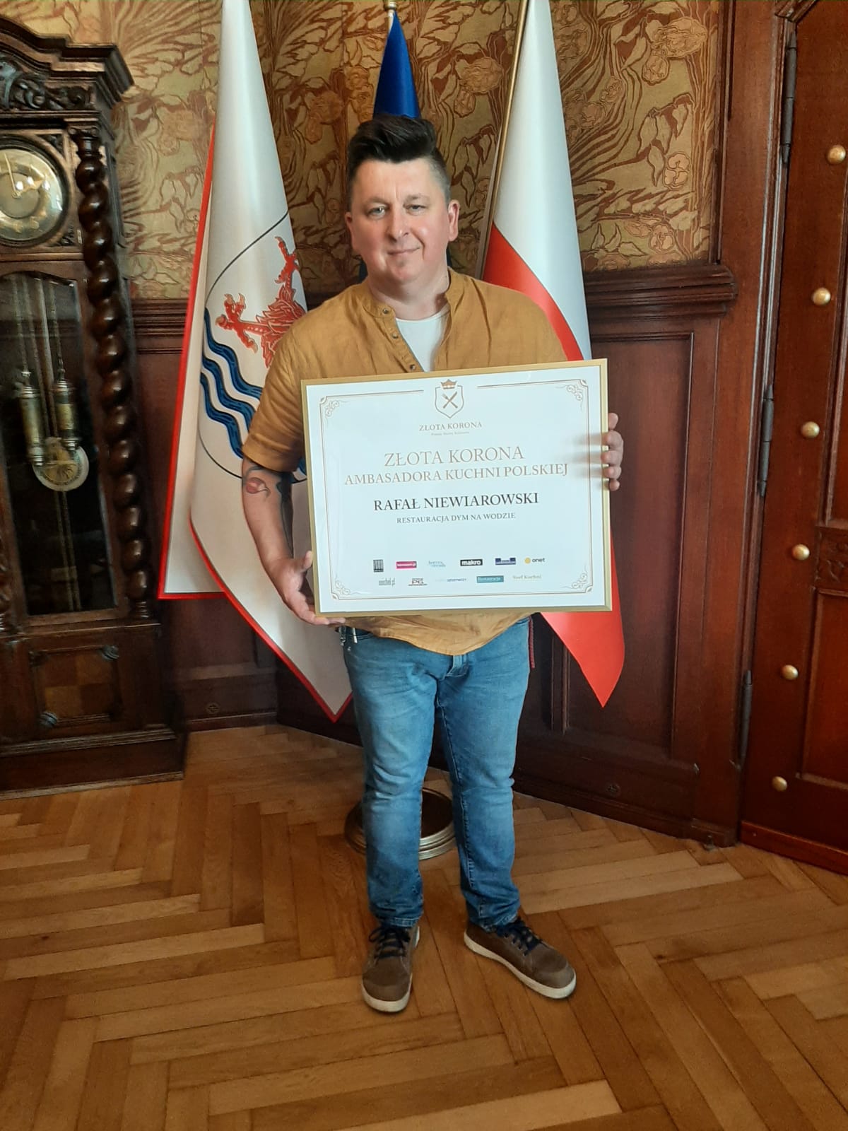 Rafał Niewiarowski trzyma ramkę z napisem Złota Korona Ambasadora Kuchni Polskiej, Rafał Niewiarowski Restauracja Dym na Wodzie