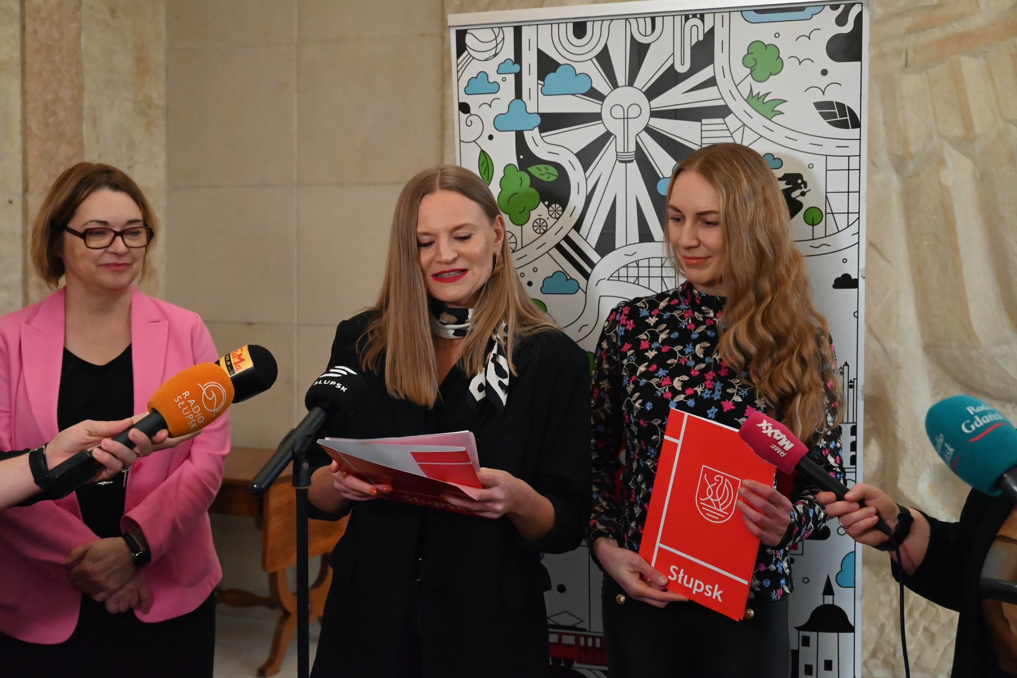 Trzy kobiety stoją  przed nimi mikrofonami przedstawicieli mediów