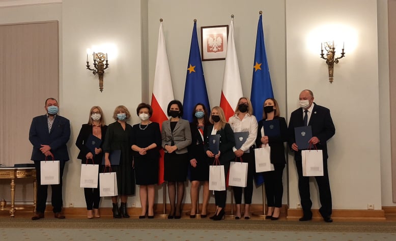 Na zdjęciu widzimy 10 osób, w tym nagrodzoną Panią Katarzynę Mulawę, w tle flagi Polski i Unii Europejskiej