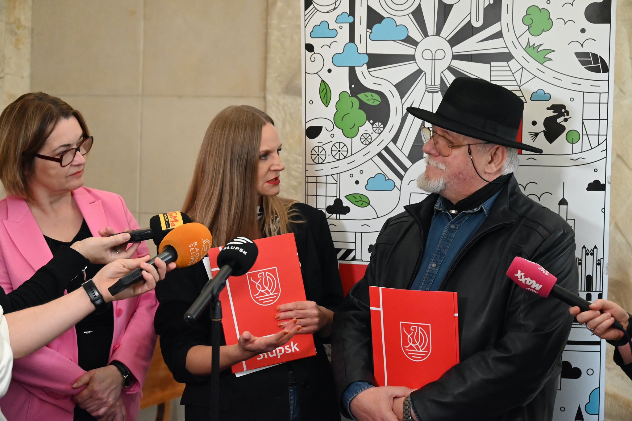 Mężczyzna i dwie kobiety stoją przed nimi mikrofony przedstawicieli mediów
