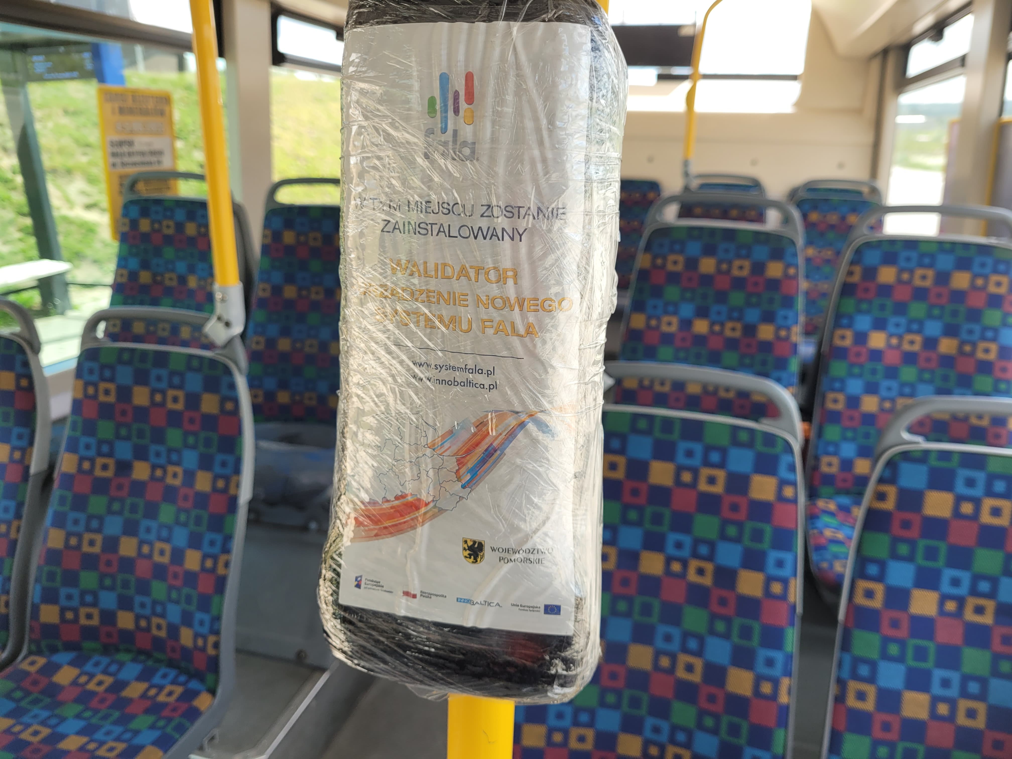 Na zdjęciu widzimy wnętrze autobusu miejskiego- siedzenia i uchwyty oraz  zafolionwany holder.