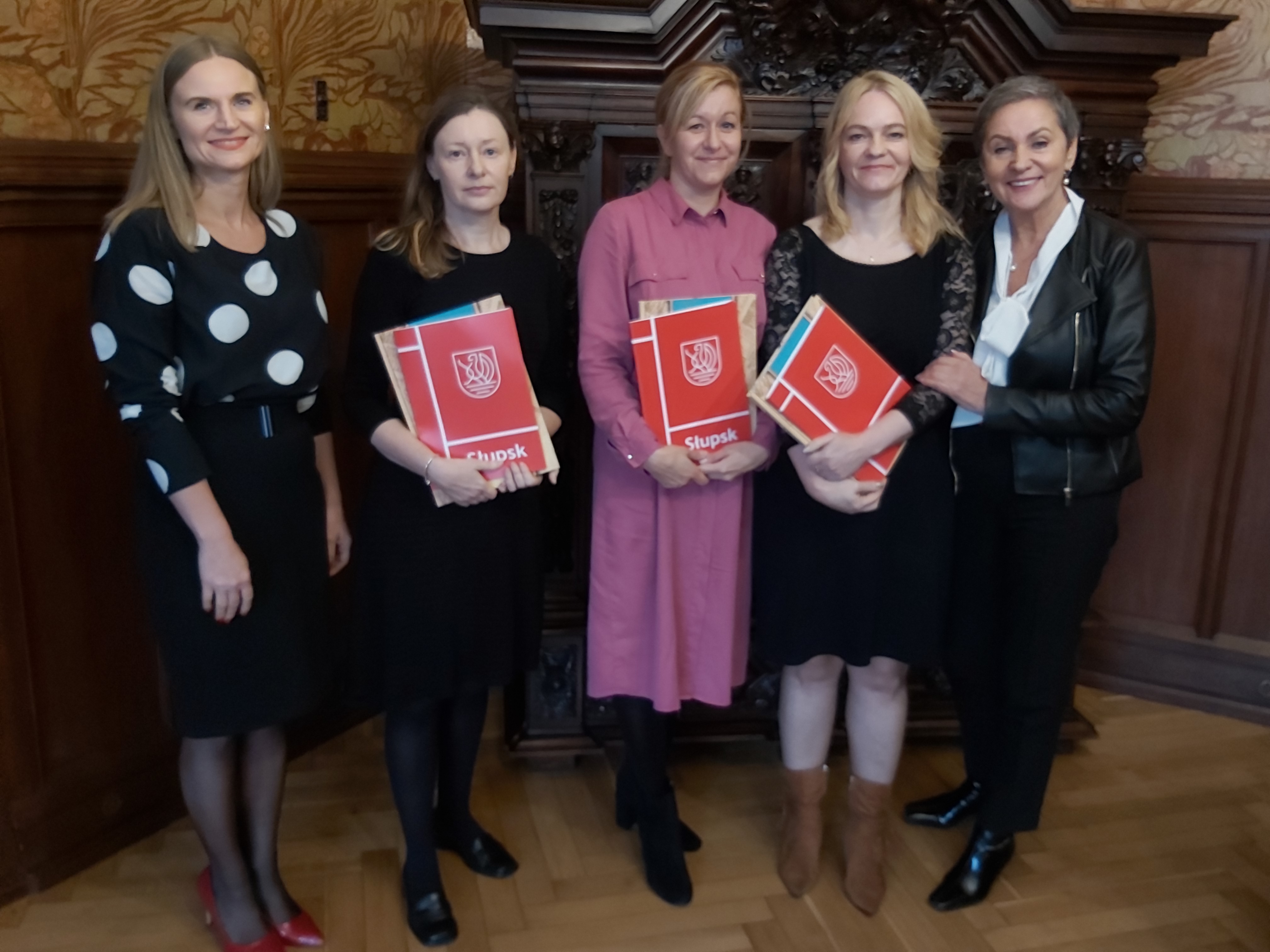 Na zdjęciu widzimy 5 kobiet, Prezydentkę oraz Wiceprezydentkę Słupska, a także trzy finalistki konkursu trzymające teczki prezydenckie z listami gratulacyjnymi