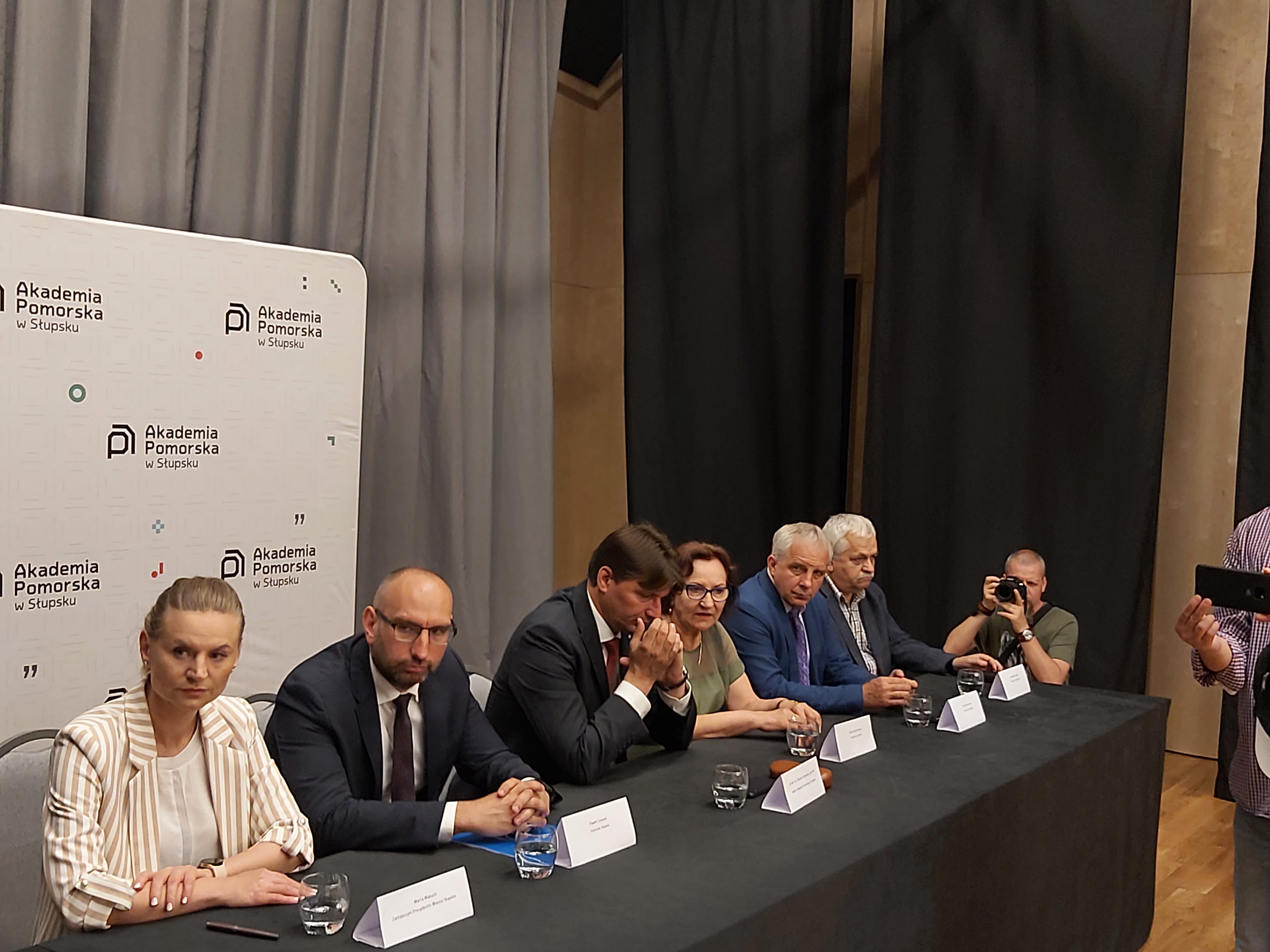 Na zdjęciu widzimy 6 osób, w tym Wiceprezydentkę Makuch i Rektora Akdademii Pomorskiej; w tle fotograf. 6 osób siedzi przy stole, na którym są m.in. szklanki z wodą