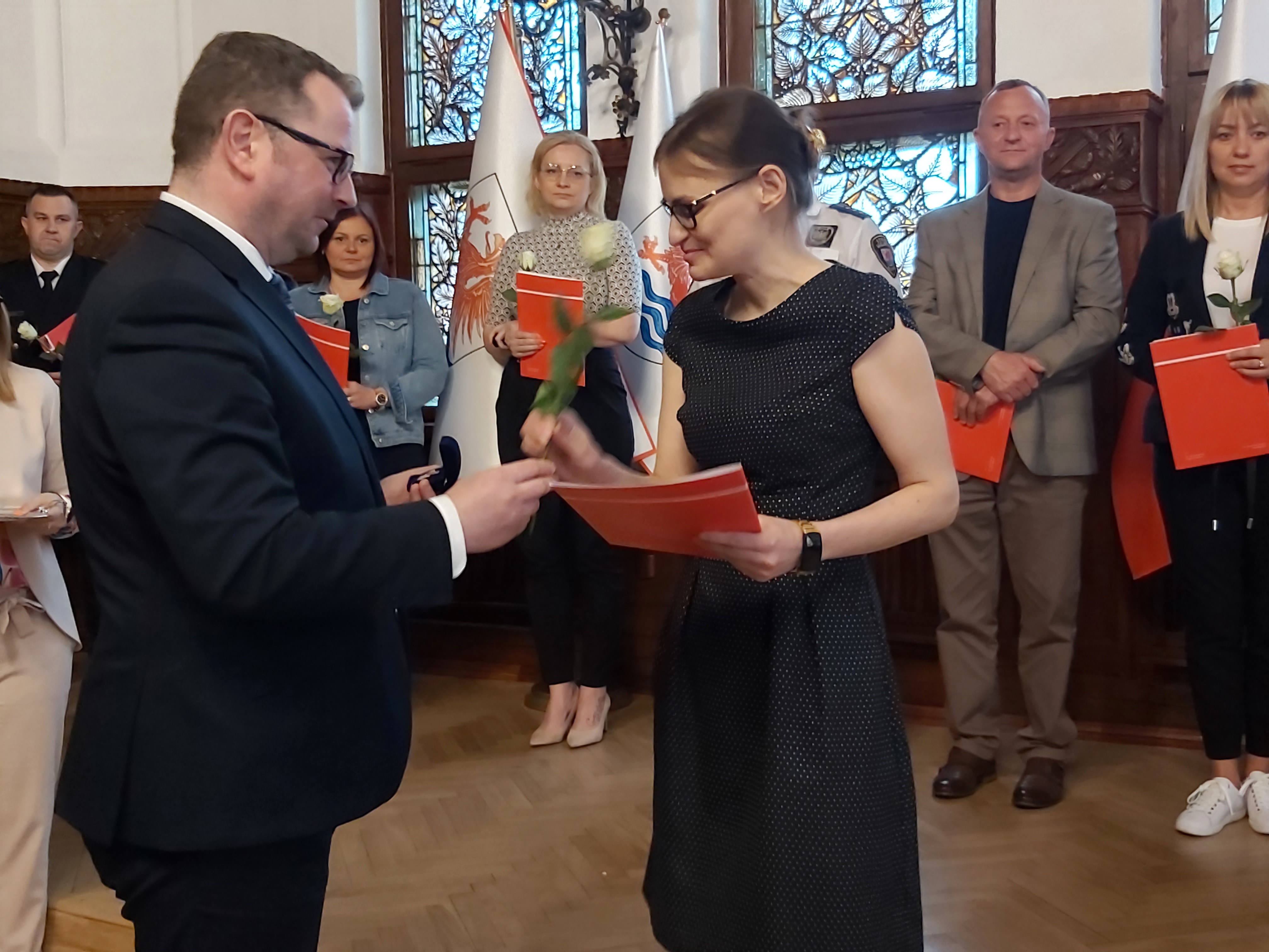 Wiceprezydent wręcza białą różę Urzędniczce , w tle inni  wyróżnieni