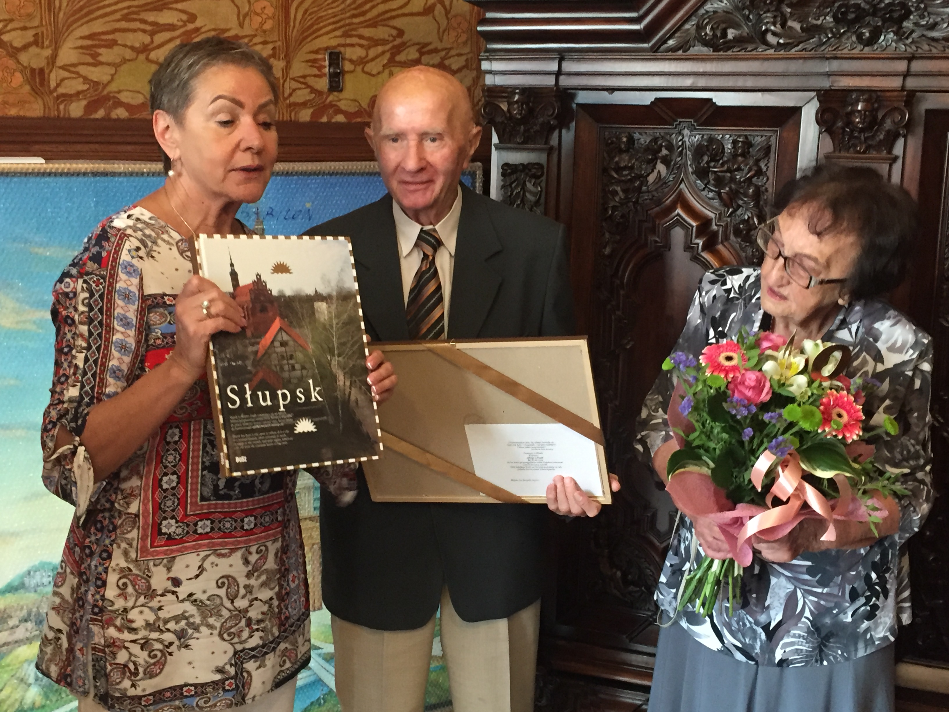Pani Prezydent trzyma Album o Słupsku, który wręcza Jubilatom, Jubilat trzyma obraz a Jubilatka kwiaty