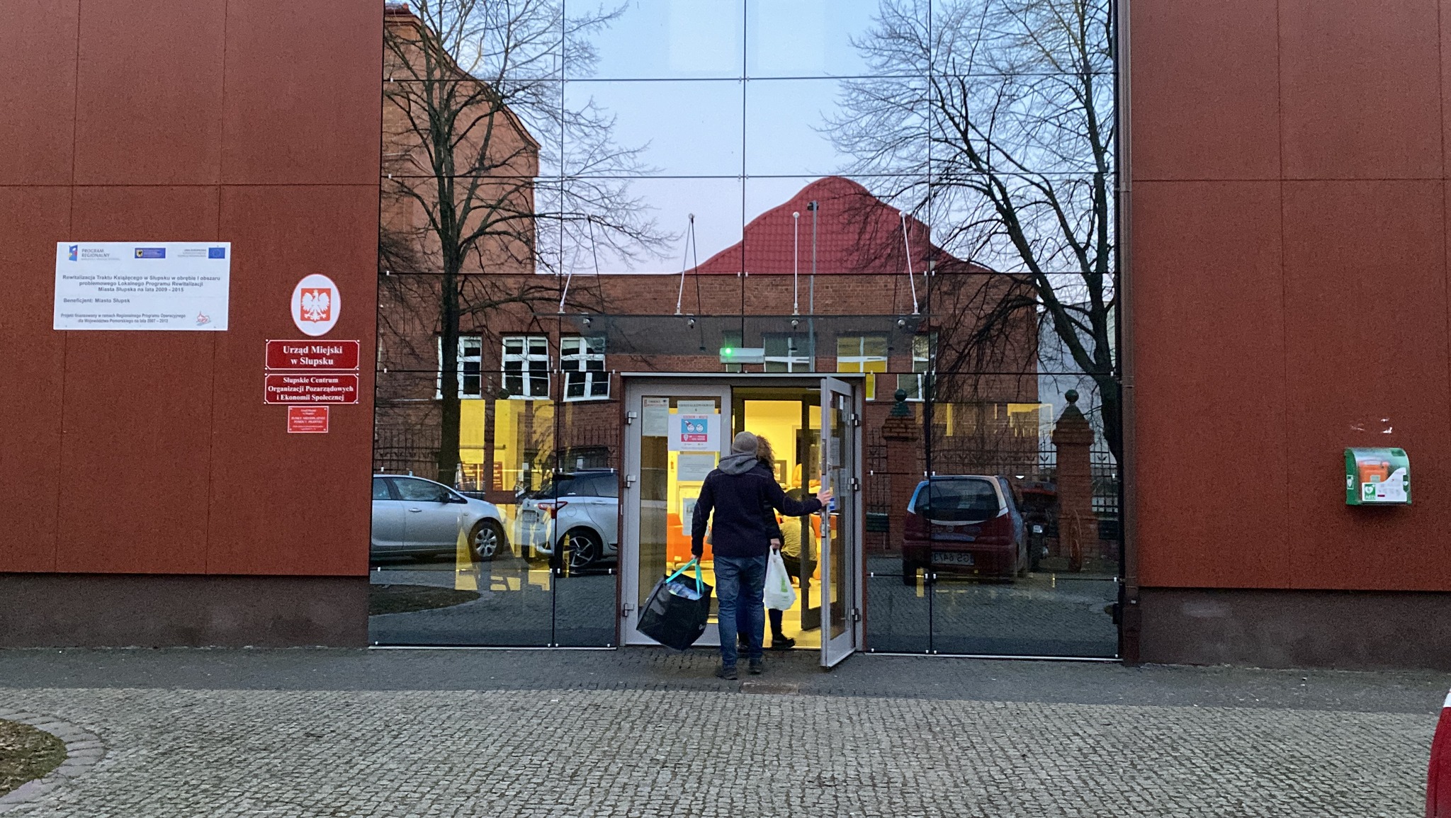 Zdjęcie z zewnątrz budynku Słupskiego Centrum organizacji Pozarządowych i Ekonomii SPołecznej, ludzie wchodzą do budynku z darami