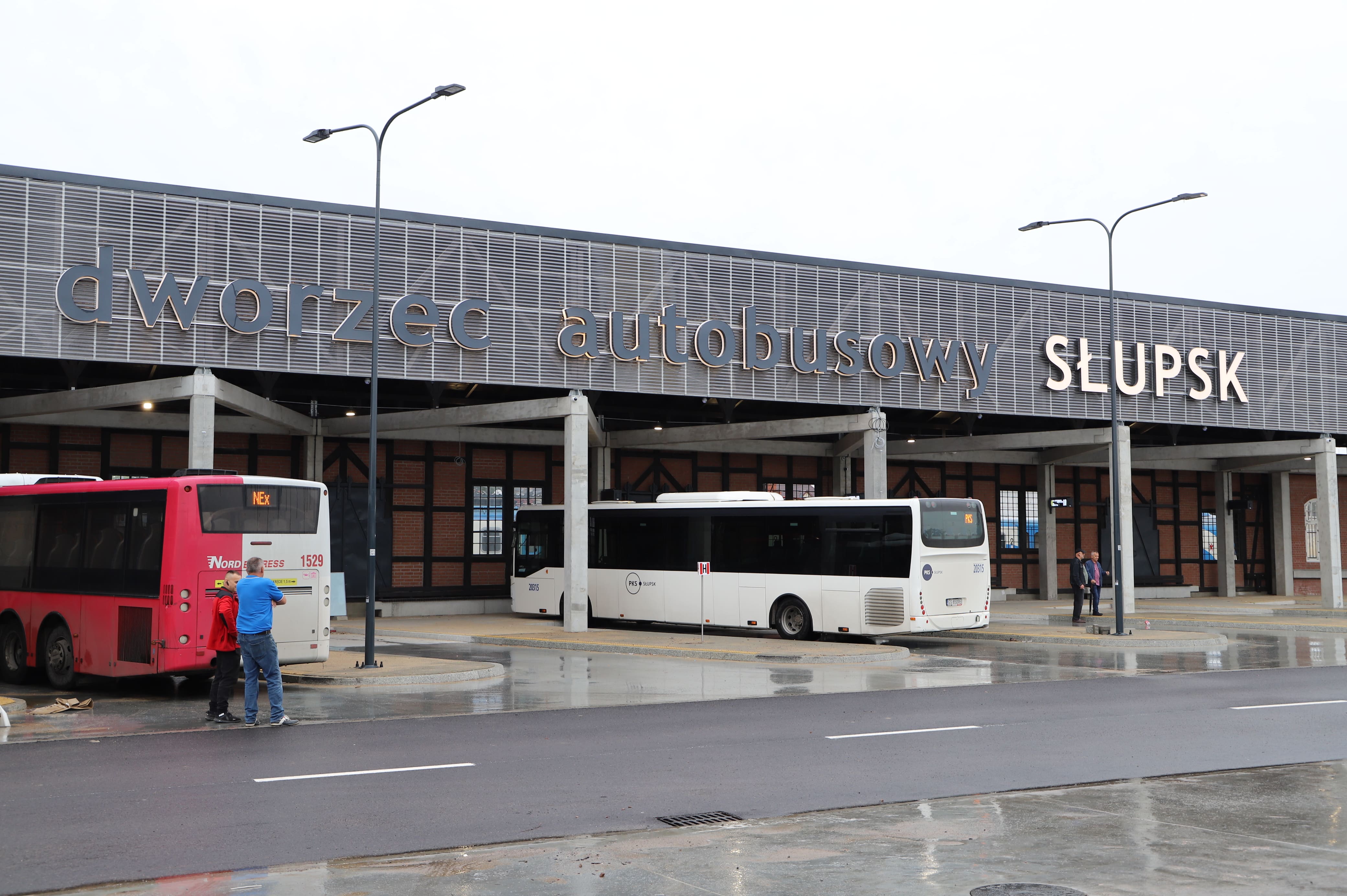 Dworzec autobusowy Słupsk - fasada dworca oraz dwa autobusy na stanowiskach przyjazdu/odjazdu, także 4 ludzi