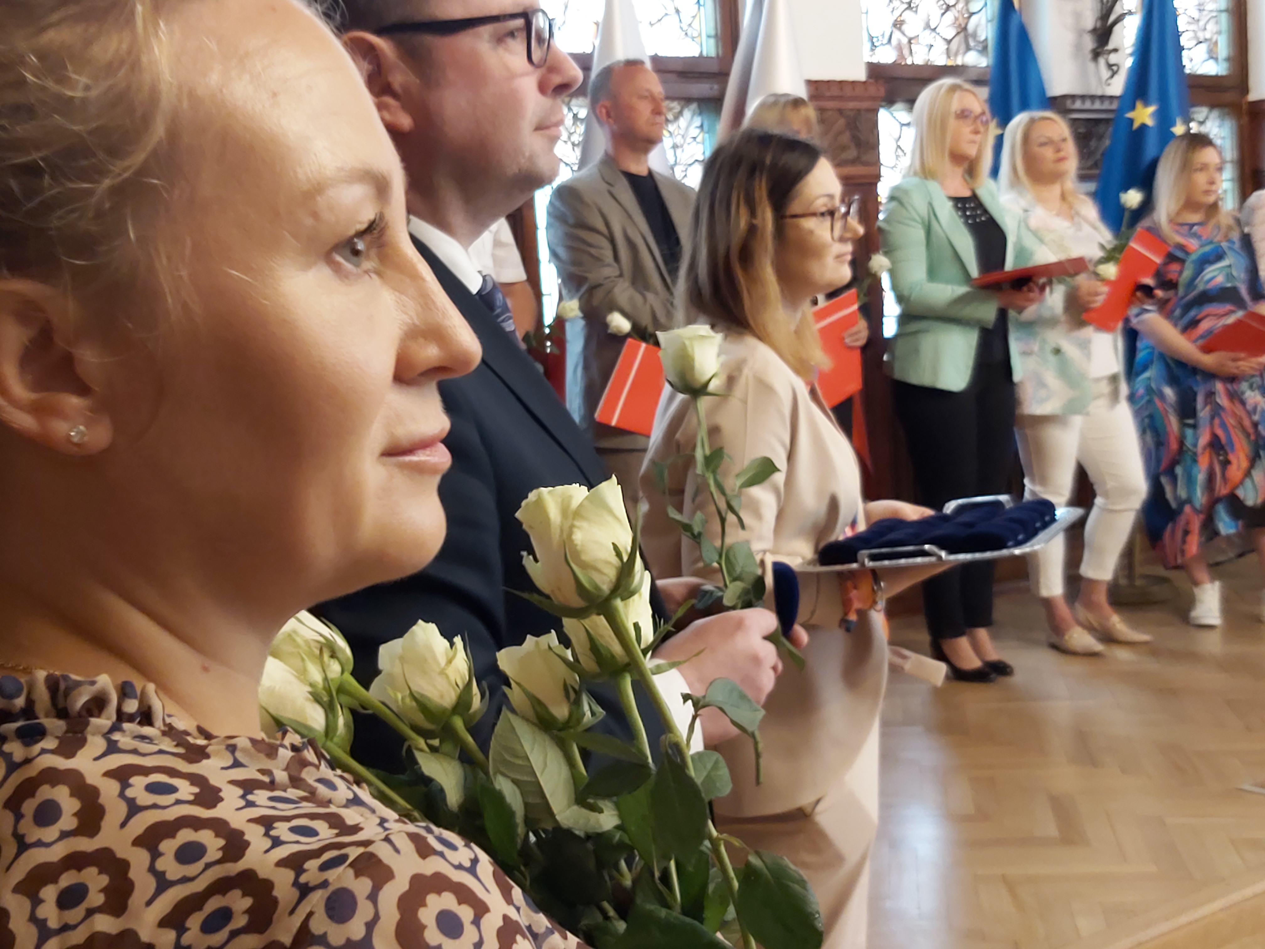 Urzędniczka trzyma białe róże, dalej Wiceprezydent Miasta i wyróżnieni pracownicy