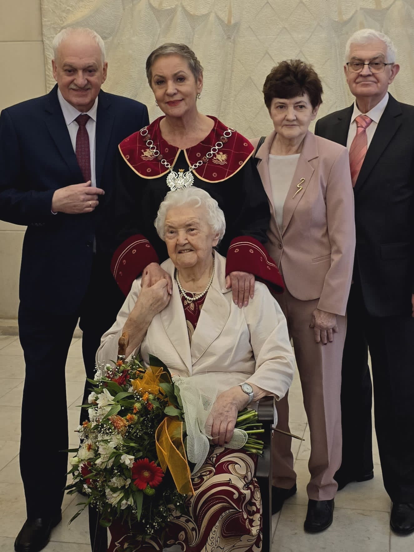 Jubilatka trzymająca kwiaty, Pani Prezydent oraz rodzina Jubilatki - 3 osoby; łącznie na zdjęciu 5 osób