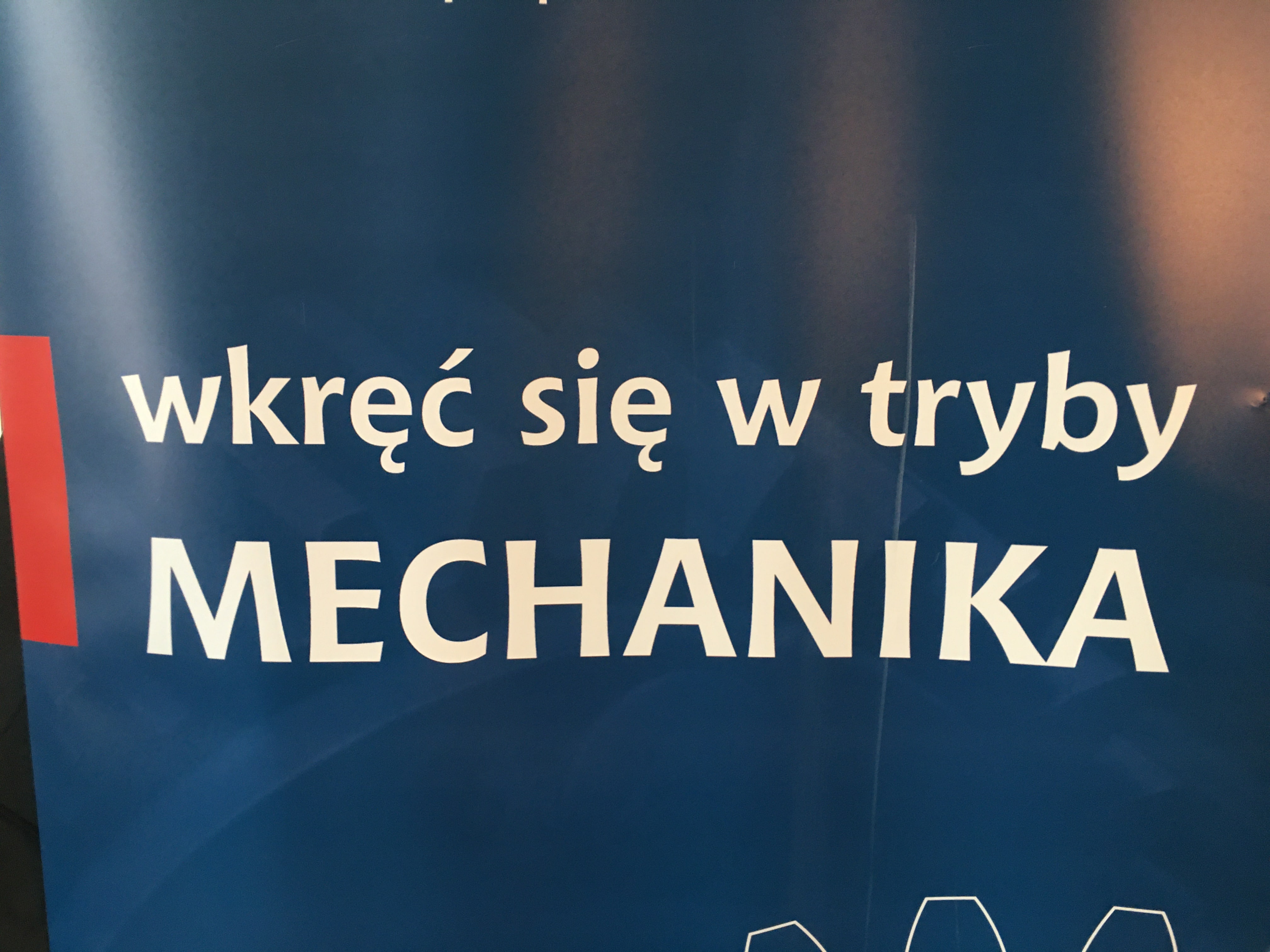 Zdjęcie fragmentu rollupu szkoły z napisem "wkręć się w tryby mechanika"