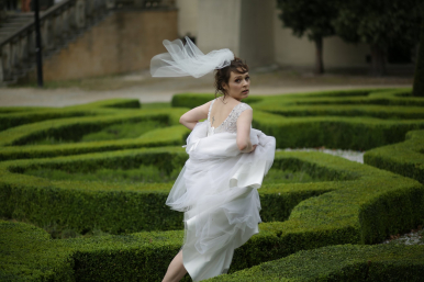 Panna młoda w białej sukni biegnie przez niski, zielony labirynt z bukszpanu