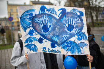 osoby trzymające plakat z niebieskim sercem, odbitymi dłońmi oraz niebieskimi parasolami