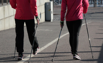 Obraz Sirpa P z Pixabay. Obraz przedstawiający dwie osoby spacerujące po asfalcie z kijami do nordic walking. Widoczne tylko nogi, tłów i ręce.