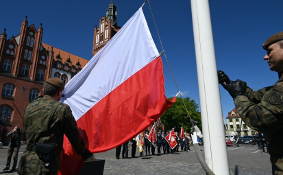 Żołnierze RP wieszający flagę RP, w tle ratusz i poczty sztandarowe