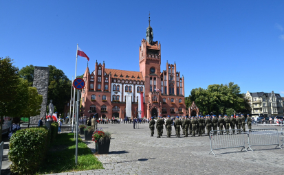 zdjęcie poglądowe, w tle ratusz, na pl. Zwycięstwa Wojsko RP, uczestnicy ur. z lat ubiegłych, pomnik Żołnierza Polskiego i miejska zieleń