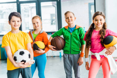 na zdjęciu czworo dzieci - dwoje chłopców i dwie dziewczynki. Dzieci ubrane na sportowo, w rękach trzymają piłki