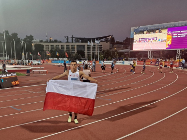 Marek Zakrzewski z biało-czerwoną flagą na bieżni stadionu.