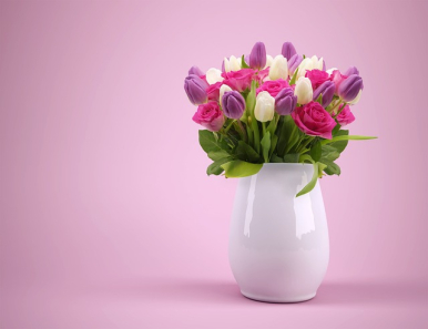 Na zdjęciu widzimy jasny wazon, do którego włożony jest bukiet kwiatów koloru różowego, kremowego i fioletowego. Tło zdjęcia jest rózowe.
