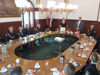 Na zdjęciu widzimy kilkanaście osób zgromadzonych wokół owalnego stołu, na którym znajdują się termosy z kawą i filiżanki.