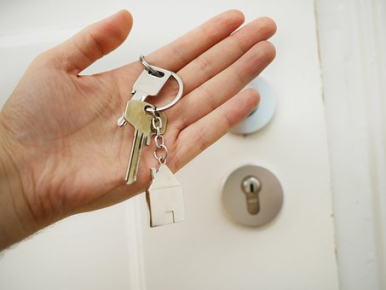 Na zdjęciu widzimy dłoń trzymającą pęk kluczy w tle jasne drzwi