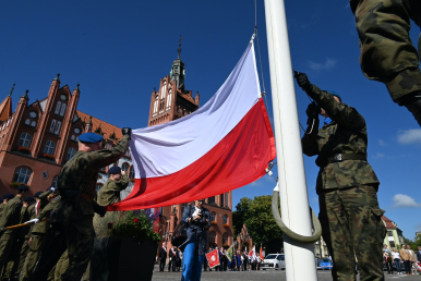Żołnierze wieszający flagę państwową na maszt- w tle ratusz słupski