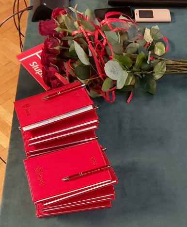 na stole leżą kalendarze z długopisami oraz bukiet róż