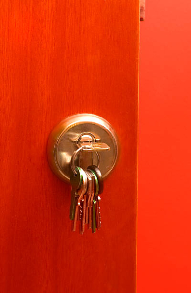 Zdjęcie przedstawia czerwone drzwi wejściowe z pękiem kluczy w zamku