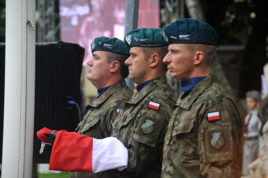 Trzech żołnierzy  w mundurach trzymających flagę RP