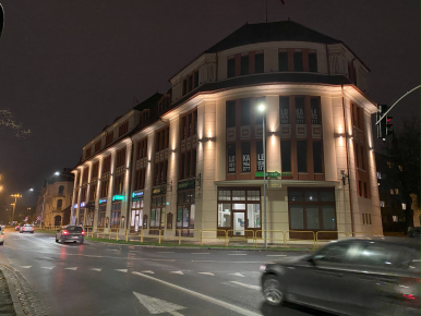 Zdjęcie poglądowe ukazujące ulicę Anny Łajming i nieruchomości przy drodze, jak Złota Kamienica. Na jezdni auta, zdjęcie nocne, lampy i światła w tle