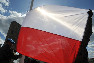 Flaga Rzeczypospolitej Polskiej trzymana przez żołnierzy na tle niebieskiego nieba