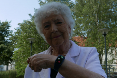 Zdjęcie przedstawia seniorkę z opaską SOS na ręku.