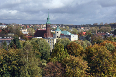 Na zdjęciu widzimy kościół św. Jacka, ceglaną budowlę ze strzelistą wieżą, oprócz tego dużo zieleni, drzew i panoramę miasta Słupska