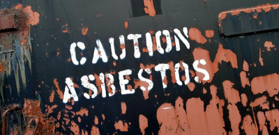 Napis "Uwaga azbest" po angielsku na czarno-brązowym tle