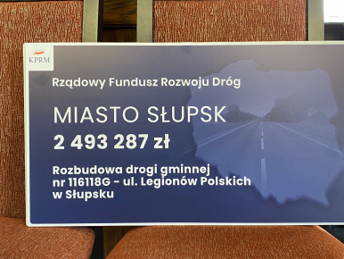 na zdjęciu widzimy symboliczny czek z napisem Rządowy Fundusz Rzwoju Dróg Miasto Słupsk 2 493 287 zł Rozbudowa drogi gminnej nr 116 118 G- ul. Legionów Polskich w Słupsku