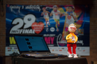 Na pierwszym planie rozłożony laptop, obok stojąca figurka Jurka Owsiaka wykonana z włóczki w tle plakat z napisem 29. Finał Wielkiej Orkiestry Świątecznej Pomocy