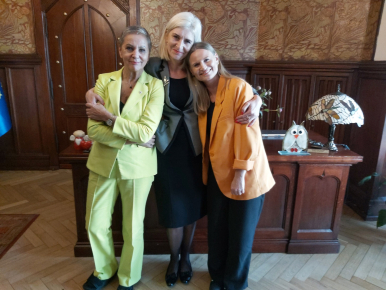 Beata Pawlicka z Prezydentkami Krystyną Danilecką-Wojewódzką i Martą Makuch, w tle biurko m.in. z bukietem kwiatów
