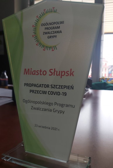 Na zdjęciu widzimy statuetkę z napisem MIASTO SŁUPSK PROPAGATOR SZCZEPIEŃ PRZECIWKO COVID-19, OGÓLNOPOLSKI PROGRAM ZWALCZANIA GRYPY,23 WRZEŚNIA 2021 R