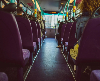 Na zdjęciu widzimy wnętrze autobusu miejskiego- siedzenia i uchwyty oraz  ramiona pasażerów