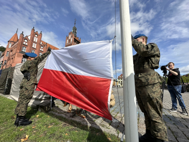 Żołnierze wieszający flagę Polski , na tle ratusz