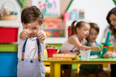 Na zdjęciu widzimy chłopca z podniesionymi kciukami do góry, w tle dwoje dzieci i nauczycielka