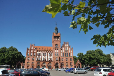 ratusz, przed ratuszem zaparkowane na parkingu samochody, błękitne niebo