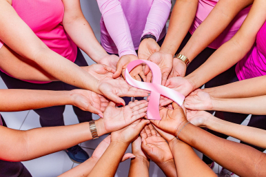 Grafika przedstawia dłonie kobiet w różowych bluzkach, ułożone w okrąg, trzymające dużą różową wstążkę. Fot. Pixabay.